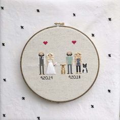 a cross stitch wedding picture with the couple and their dog on each side, framed in white fabric