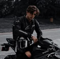 a man sitting on top of a motorcycle next to a road with trees in the background