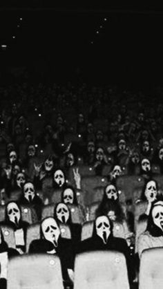 people wearing masks sit in rows at an auditorium with their faces painted on the seats