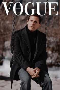 a man sitting on a swing with his hands in his pockets while wearing a black coat