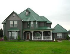 a large gray house sitting in the middle of a lush green field on a cloudy day