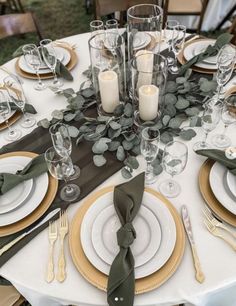 the table is set with white and gold plates, silverware, green napkins and candles