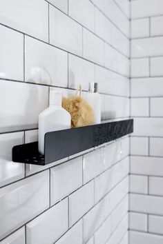 a teddy bear sitting on top of a shelf in a tiled wall next to soap dispensers