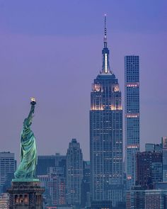 the statue of liberty is lit up in front of the empire building and skyscrapers