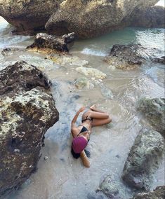 a woman laying on top of a sandy beach next to the ocean with rocks in the background