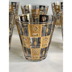 a set of six glass cups sitting on top of a white table covered in gold and black designs