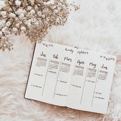 three calendars sitting on top of a fluffy white blanket next to a vase with flowers