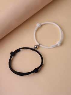 a black cord bracelet with a silver bead on it and a roll of paper in the background