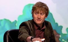 a man sitting in a chair with his hand on the remote and looking at the camera