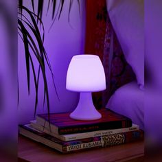 a lamp sitting on top of a stack of books next to a purple light in a bedroom