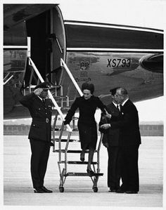 three men in suits and ties standing next to an airplane on the tarmac with another man walking up