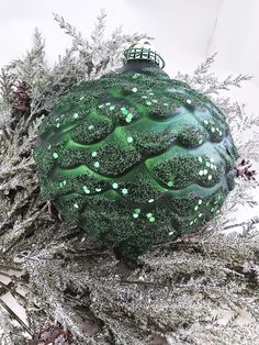 a green ornament sitting on top of a tree covered in frosted branches