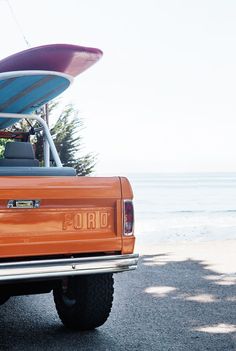 an orange pick up truck with a surfboard on the roof and back end in front of it