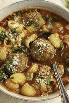 a bowl filled with pasta and meatballs covered in grated parmesan cheese