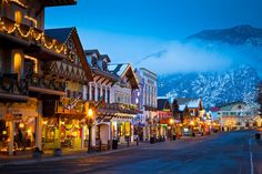 a street lined with buildings and christmas lights in front of a snow covered mountain range