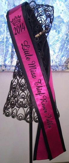 a pink and black sash on top of a metal stand with a blue wall in the background