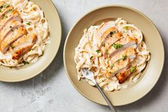 two plates of pasta with chicken and parmesan cheese on the side, one has a fork in it