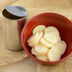 a red bowl filled with sliced up apples next to a can of canned drink on a burlap cloth