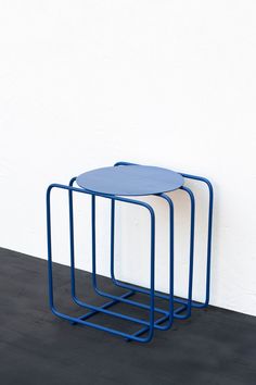 two blue tables sitting next to each other on top of a black floor in front of a white wall