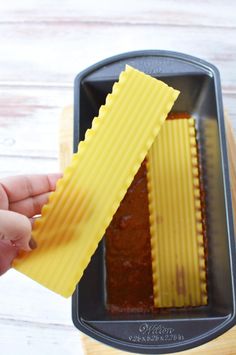 someone is holding up some food in a pan with noodles on it and another piece of yellow paper sticking out of the top