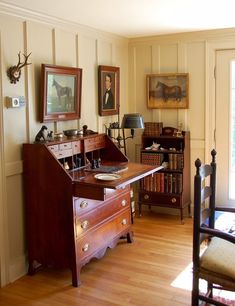 an antique desk in the corner of a room with pictures on the wall and other antiques