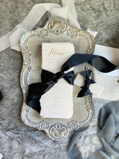 the wedding stationery is laid out on top of silver and white paper with black ribbon