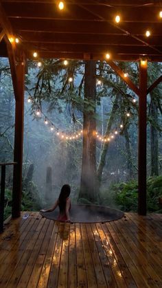 a woman sitting on a wooden deck in front of a tree with lights strung from it