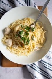 a white bowl filled with pasta and meat on top of a wooden cutting board next to a fork