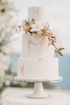 a white wedding cake with flowers on top and greenery in the middle is sitting on a table