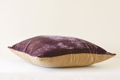 a purple velvet pillow sitting on top of a white bed