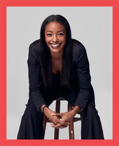 a smiling woman sitting on top of a wooden chair with her legs crossed in front of her