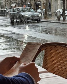 a person sitting at a table reading a book in the rain with cars passing by