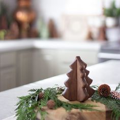 a small wooden christmas tree sitting on top of a cutting board next to pine cones