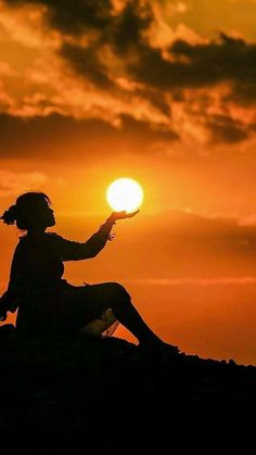 a person sitting on top of a hill with the sun setting in the sky behind them