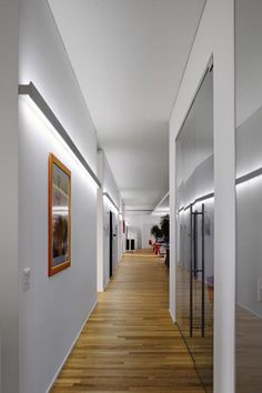 an empty hallway with white walls and wood flooring is lit by recessed lighting