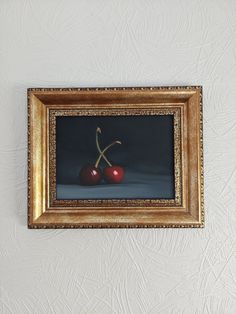 two cherries in a gold frame hanging on the wall next to a white wall