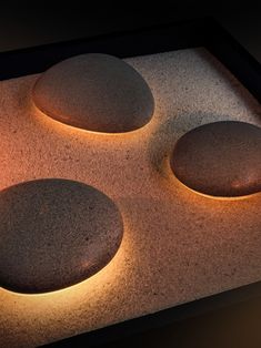 three rocks sitting on top of a stone covered counter next to a lit up light