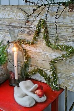 a red table topped with a candle and two apples next to a vase filled with greenery