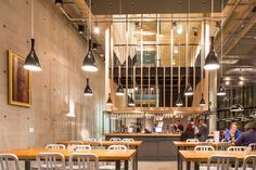 an empty restaurant with wooden tables and metal chairs in front of the counter, people are standing at the bar