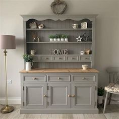 a grey hutch with some plants on top and other items in the cupboards