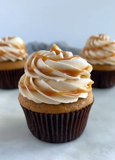 three cupcakes with white frosting and caramel swirl on top sitting on a table