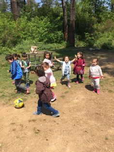 a group of children playing soccer on a dirt field with trees in the back ground