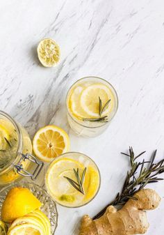 three glasses filled with lemonade and rosemary garnish next to sliced lemons