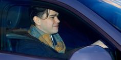 a man sitting in the passenger seat of a car wearing a blue coat and scarf