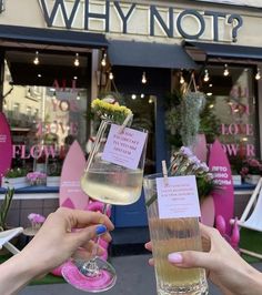 two people holding up wine glasses in front of a flower shop that says, why not?