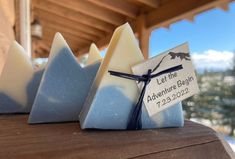 three soap bars sitting on top of a wooden table next to snow covered mountains and trees