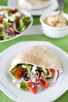 a pita filled with vegetables and sauce on top of a white plate next to a bowl of hummus