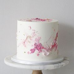 a white cake with pink flowers on it sitting on top of a wooden stand next to a wall