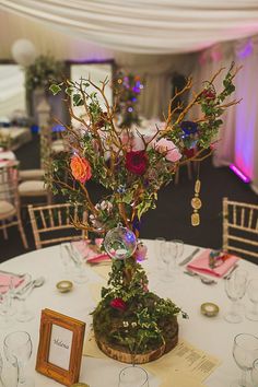 an arrangement of flowers in a vase on top of a round table with place settings