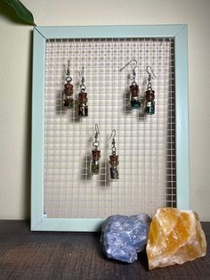 two pieces of jewelry sitting on top of a wooden table next to a rock and wire frame